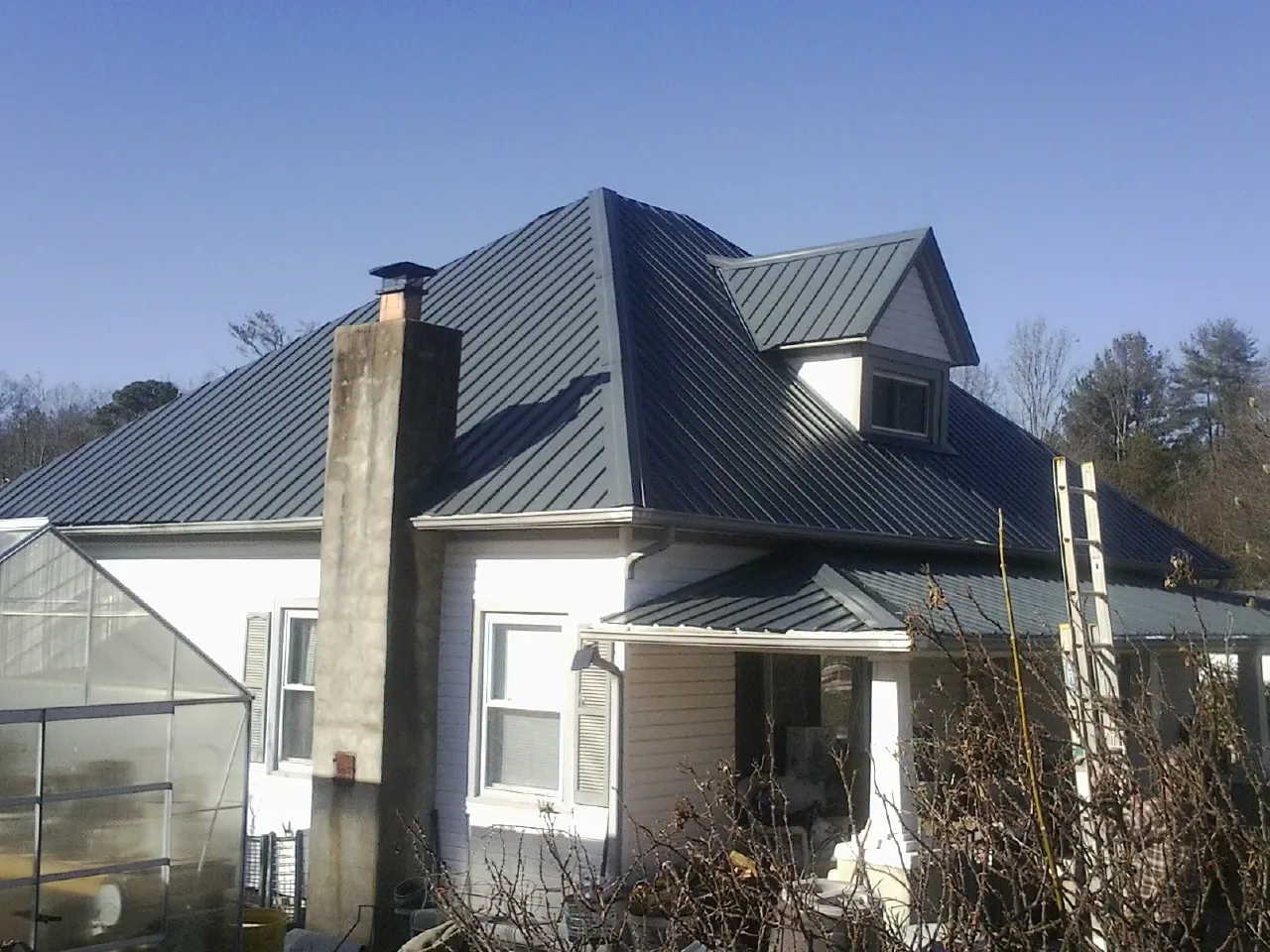 Dark blue standing seam metal roof on a white farmhouse with dormer — Slate & Tile Roof Repair by Roofing Brothers in Paxton