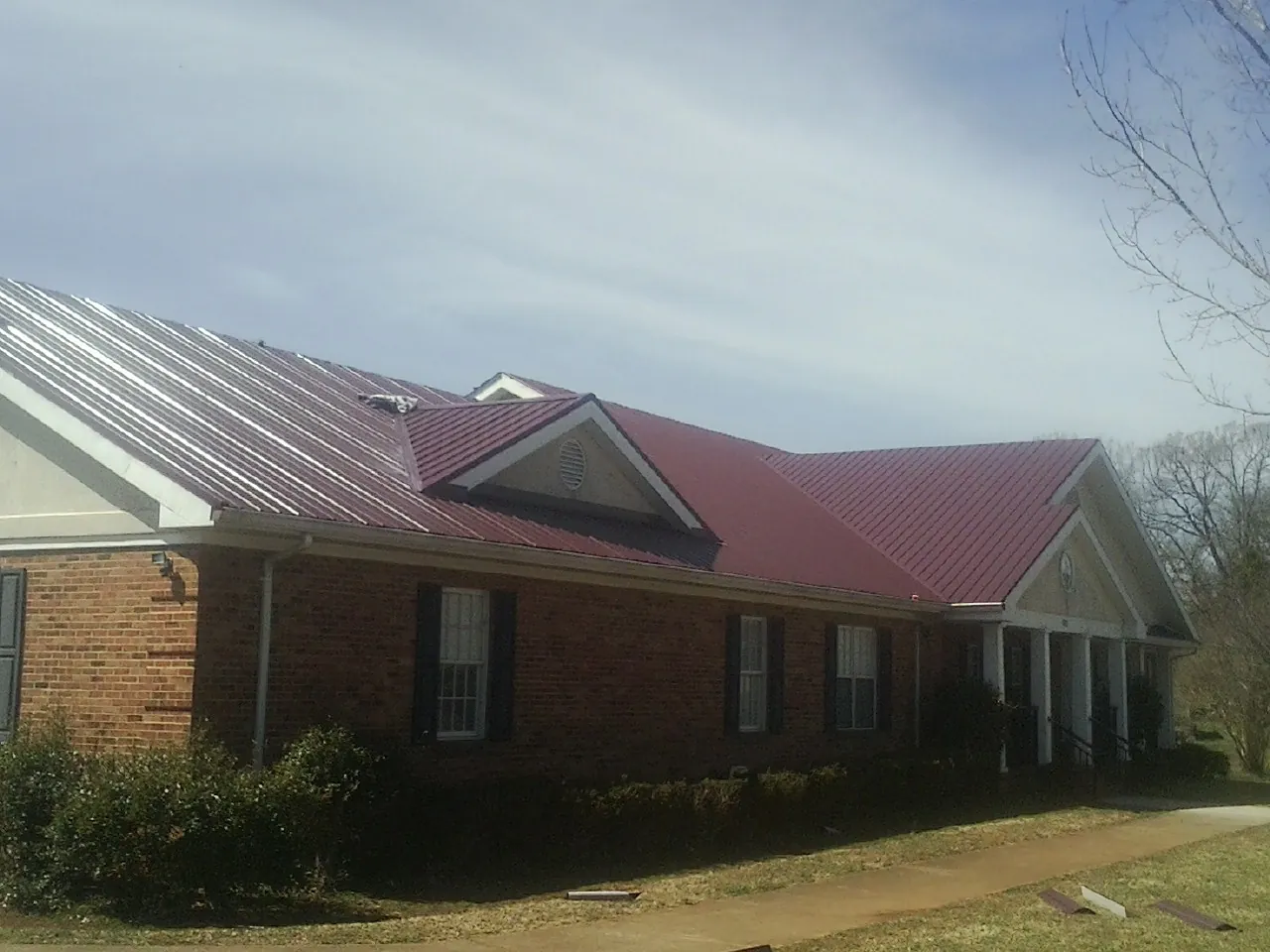Red metal roof with gabled entries on a long brick building, from a Hail Damage Roof Repair job in Paxton