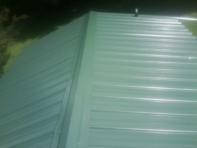 New green metal panels meeting at the ridge of a roof — Flat Roof Repair work by our crew in Paxton