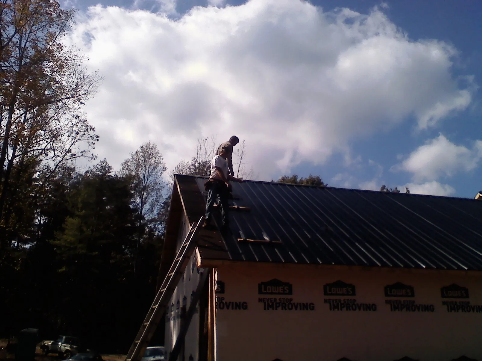 Roofer fastening dark metal panels high against a cloudy sky, from a Roof Inspection job in Paxton